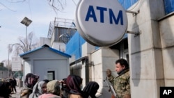 An Afghan security guard holds his AK-47 rifle, as women lineup outside an ATM machine to withdraw money, in Kabul, Afghanistan, Feb. 8, 2022.