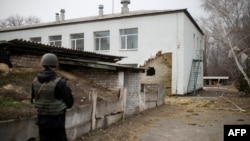 A Ukrainian soldier stands next to a damaged building housing a kindergarten after it was shelled, in the town of Stanytsia Luhanska, Luhansk region, Ukraine, Feb. 17, 2022.