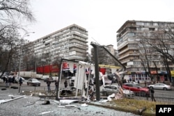 People are seen outside the cordoned-off area around the remains of a shell in a street in Kyiv, Feb. 24, 2022.