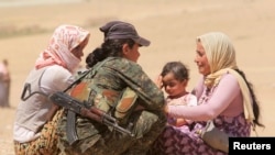 Displaced people from the minority Yazidi sect, fleeing violence from forces loyal to the Islamic State in Sinjar town, get help from a member of the YPG near the Syrian border.