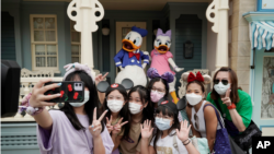 在香港迪士尼樂園，戴著口罩的遊客與標誌性卡通人物唐老鴨和黛絲鴨自拍。 （2020年9月25日）