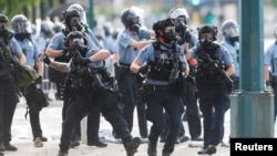 Seorang petugas kepolisian melempar tabung-tabung asap untuk membubarkan massa yang berdemo dekat kantor polisi Minneapolis, AS, 27 Mei 2020, setelah kematian seorang Afrika-Amerika, George Floyd, saat diamankan polisi. (Foto: Reuters) 