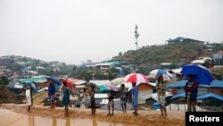 Un grupo de rohingyas espera con sombrillas bajo un aguacero en un campo de refugiados en Bangladesh.