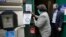 A voter, left, places a ballot in a secure box as Providence City Clerk Shawn Selleck, right, looks on, Tuesday, June 2, 2020, in Providence, R.I. Because so many voters asked for mail ballots, state electoral officials say mail ballots can be dropped off