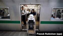Tomomi Ota pulls a cart loaded with her humanoid robot Pepper as she boards a subway train in Tokyo, Japan, 27 June 2016.
