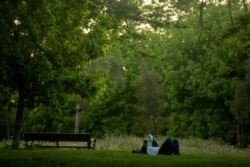 A man holds a face mask as he rests in a public park in Madrid, Spain, May 6, 2020.