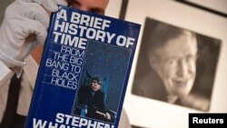 Fine-art handler Tom Richardson poses with a copy of A Brief History of Time which, has a thumb-print inside by author British theoretical physicist Stephen Hawking, ahead of an auction of items from Hawkinsg' personal estate at Christie's in London, Brit