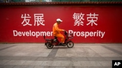 FILE - A maintenance worker rides a scooter past banners reading "Development" and "Prosperity" in English and Chinese on a street in central Beijing, July 15, 2015.