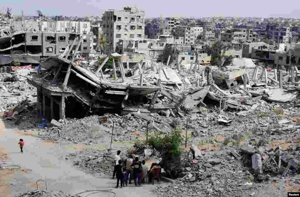 Palestinians sit next to the rubble of houses destroyed in Israel's military offensive, amid the ongoing conflict between Israel and Hamas, in Khan Younis in the southern Gaza Strip.