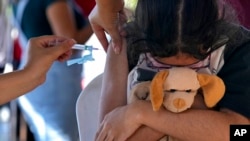 FILE - A girl hugs her stuffed toy as she gets a shot of the Pfizer COVID-19 vaccine at a community health center, in Brasilia, Brazil, Jan. 16, 2022. (AP Photo/Eraldo Peres)
