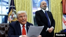 U.S. President Donald Trump reads about tariffs on steel and aluminum, as Howard Lutnick stands in the background, in the Oval Office of the White House in Washington, Feb. 10, 2025. 