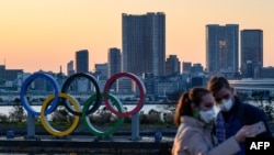 People wear face masks as they take pictures in front of the Olympic Rings at the Odaiba Seaside Park in Tokyo on March 6, 2020. - Construction of all new permanent venues for the Tokyo 2020 Olympics and Paralympics is now complete, organisers said…