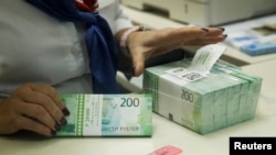 FILE - A cashier holds new 200 ruble banknotes in a bank in Moscow, Nov. 21, 2017. 