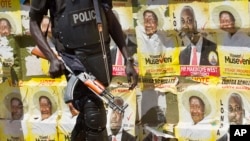 An armed Ugandan riot policeman is seen on patrol against the backdrop of campaign posters for long-time President Yoweri Museveni, as well as local members of Parliament, on a street in Kampala, Uganda, Feb. 17, 2016.
