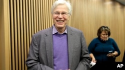 Cora Rose, anjing yang dua kaki depannya telah diamputasi berusaha menjaga keseimbangan badannya saat mengamati Zach Skow memperbaiki roda keretanya di sebuah jalan di Washington, D.C.