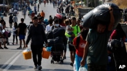 FILE - Migrants carry their belongings as they flee a road leading from Moria to the capital of Mytilene, on the northeastern island of Lesbos, Greece, Sept. 17, 2020. 