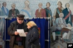 La gente examina una papeleta en un colegio electoral ubicado en una escuela durante las elecciones presidenciales en San Petersburgo, Rusia, el sábado 16 de marzo de 2024, con una pintura que representa a la zarina rusa Catalina II y sus contemporáneos en la pared.